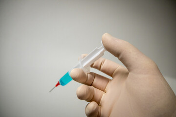 a hand with a glove holds a medical syringe with blue liquid