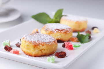 Cottage cheese pancakes with raisins and candied fruits on a white plate, side view