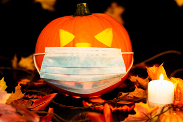 Jack o lantern medical face mask candle on adark and yellow maple leaves background and with dry leaves,