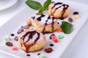 Cottage cheese pancakes with raisins, candied fruits and chocolate on a white plate, top view