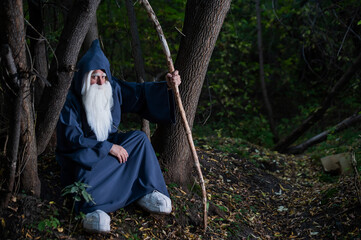 A wizard with a long gray beard and a cloak in a deep forest. An elderly man in a witcher costume