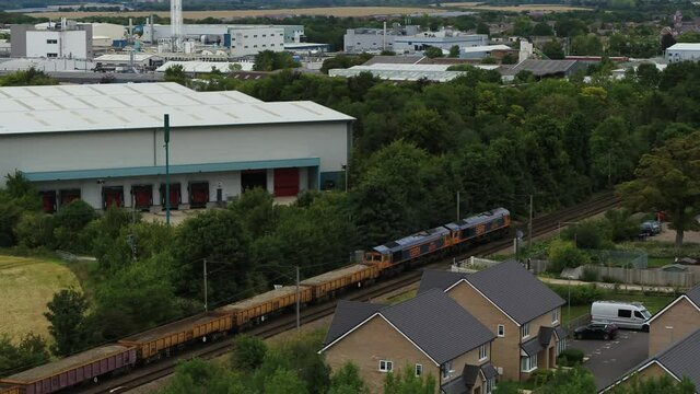 Aerial view tracking a freight train with a rising reveal of the town of Royston in England, UK