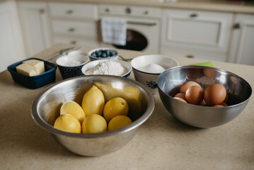 Eggs, lemons, two pieces of butter, blueberries, wheat flour, almond flour, and sugar are preparing for the lemon meringue tart in the kitchen.