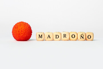 The word Madroño in wooden cubes letters next to strawberry tree fruit on white background isolated white background