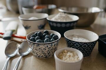 A close photo of blueberries, wheat flour, almond flour, sugar, powdered sugar which in cups are preparing for cooking in the kitchen.