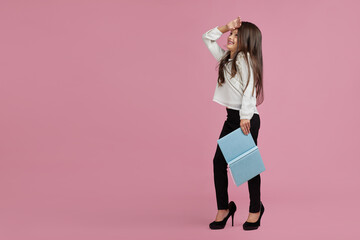 cute fashionable little child girl in oversized mother's shoes holding notebook on pink background. child playing tired and very busy businesswoman. copy space for text