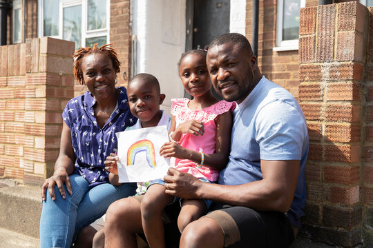 Portrait happy family with rainbow drawing on sunny front stoop