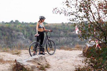 Fototapeta premium Fit young woman wearing sportswear standing with her bicycle on rocky background