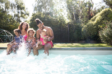 Playful family splashing in sunny summer swimming pool