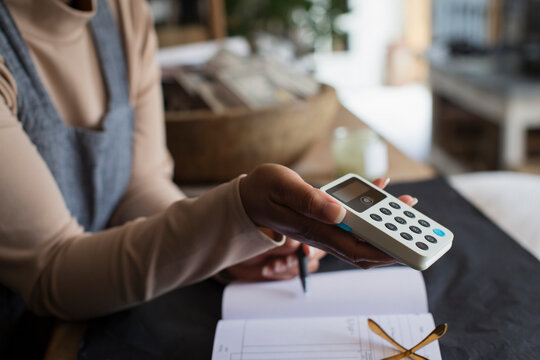 Close up female shop owner holding credit card reader at counter