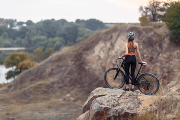 Fototapeta na wymiar Fit young woman wearing sportswear standing with her bicycle on rocky background