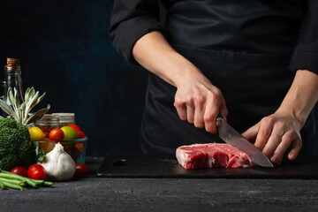Close-up view of chef cuts with knife raw steak on wooden chopped board. Backstage of preparing grilled pork meat at restaurant or hotel.