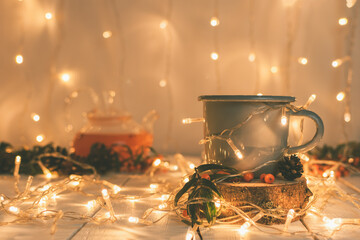 New Year's composition in warm muted colors from a cup of sea buckthorn tea on a wooden cup holder, a teapot and a festive garland.
