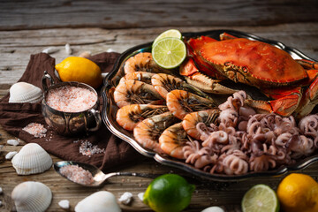 Plates with assorted seafood. Cooked crab, baby octopuses and tiger shrimps served with ice cubes, lime and seashells on rustic wooden background. Seafood concept. Delicious for gourmet.