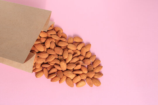 Almonds spilling out of a brown craft paper bag on a pink background. Place for text.