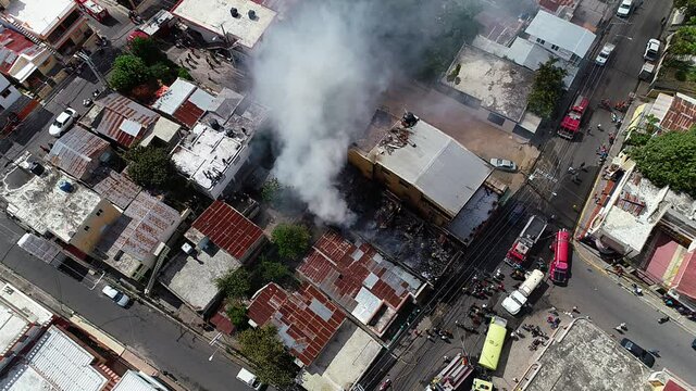 Aerial view overlooking a apartment on fire, dark smoke rising from house ruins, sunny day, in a slum area in Puerto Rico, USA - High angle, static, drone shot