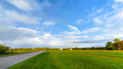 tender rainbow over a meadow and a street in the blue sky