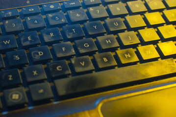 Used and filthy keyboard close up with detailed keys and letters in gradient light from blue to yellow spectrum. A modern, artistic view on old technology.