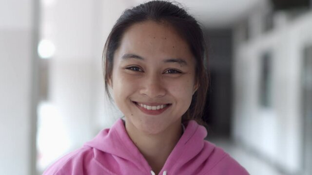A female teenage Asian high school student girl in a pink sweater is smiling happily. 
