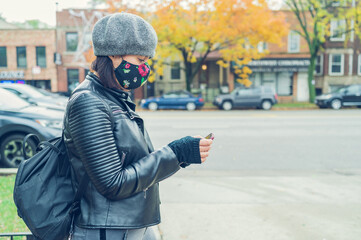 Fototapeta premium A young woman doing business with a smartphone wears a medical mask to prevent the spread of coronavirus on the street. A close-up photo of a girl with a surgical mask on her face against COVID-19.