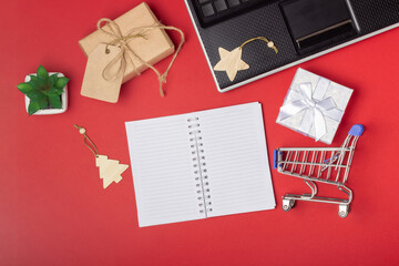 Laptop, notebook, shopping cart and boxes on a bright red background. Online shopping concept