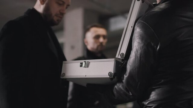 Low-angle closeup of criminal in black leather jacket on deal looking at metal briefcase with money checking