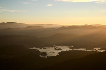 Bright golden sunlight in morning. Horizon over mountain range with stunning sunrise orange light. Maskeliya reservoir in valley. Panoramic view from Adam's Peak mountain (Sri Pada). Sri Lanka