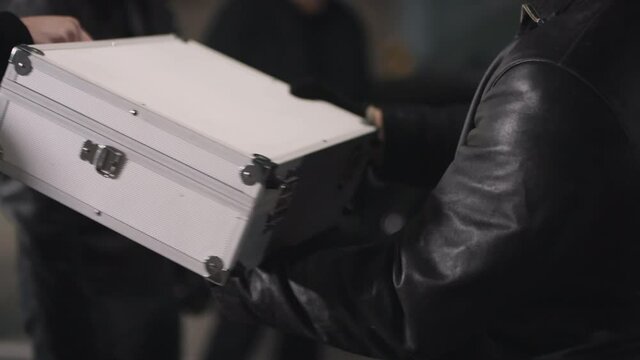 Close up of criminals hands taking metal briefcase with stacks of money at isolated parking lot