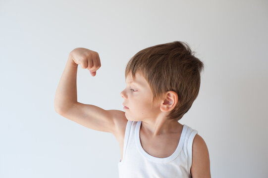 strong small child boy in white tank top showing his muscle with grimace on his face
