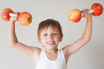 strong little caucasian funny kid child in white tank top lifting two apple dumbbells