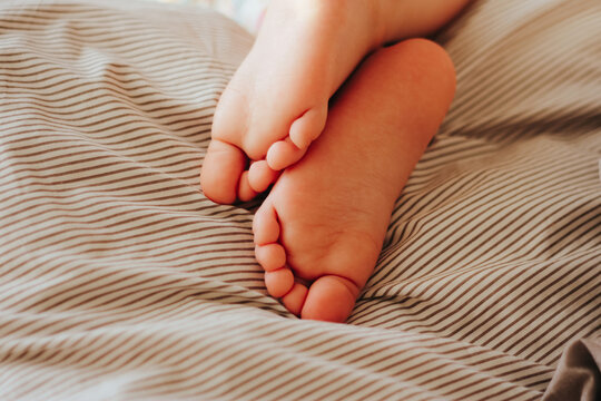 Children's Legs Stick Out From Under The Warm Blanket. Concept Of Care, Proper Sleep