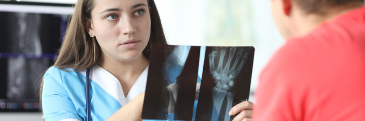 Portrait of focused radiologist discussing x-ray of hand with injured patient. Professional surgeon...