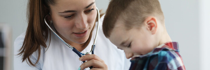 Portrait of cheerful little boy on examination by pediatrician. Doctor listening to breathing or action heart of ill patient with stethoscope. Healthcare and medicine concept