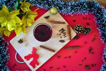 Spiced mulled wine surrounded by cinnamon sticks, cloves, star anise, a red reindeer, candy canes, tinsel in the shape of a fir branch, pins, a golden ball and golden poinsettias on a table