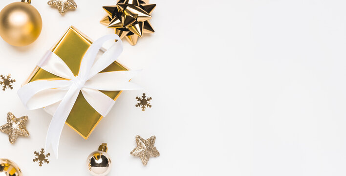 Merry Christmas and Happy Holidays greeting card background with copyspace on the right. Golden Christmas gift and decor on white background top view. Winter xmas holiday theme in flat lay