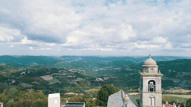 Crane down shot the main church in Roccaverano, Italy - Aerial Drone Shot Revealing the Top of the Dome, and the Bell with the mountains in the background and A Sky Full of Fluffy White Clouds