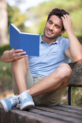 man reading a book on a bench in a park