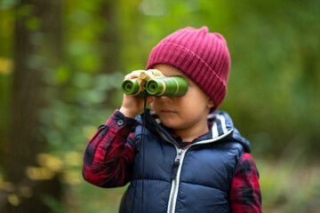 Beautiful little boy looking through binoculars wrong way