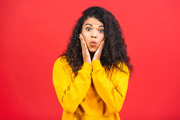 Surprised shocked amazed beautiful curly black african american woman isolated over red background.