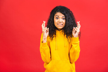 Black african american girl crossing fingers for good luck, winning lottery expectation, hope islated over red background.