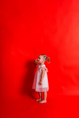 A little girl in a white dress stands sideways on a red background with space for text