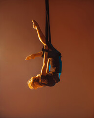 young girl in black costume is making aerial trick upside down on the beige background in photo studio in warm and cold lights, sport concept, free space © NASTYA PALEHINA