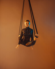 young woman in black costume is making aerial trick in longitudinal twine on the beige background...