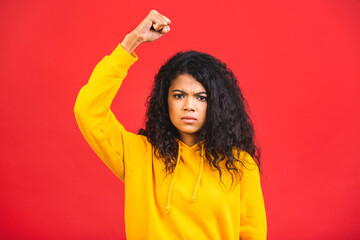 Angry brave African young woman isolated over red background raising fist and screaming. Mixed race...