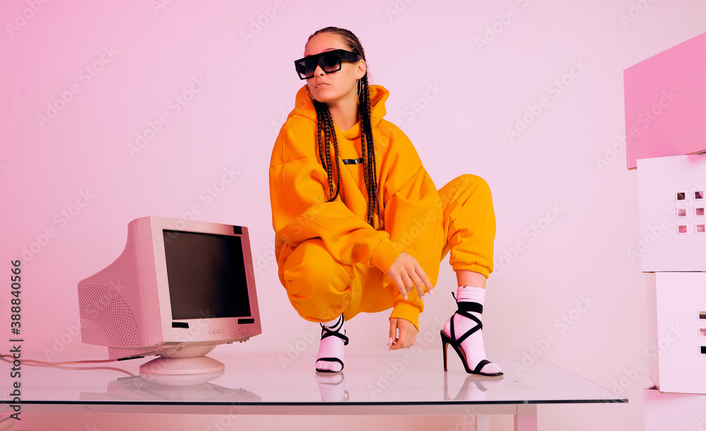 Wall mural cool asian female office worker in sunglasses on table with obsolete computer. colored light