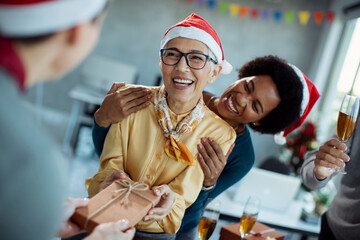 Happy businesswoman getting gift box from colleagues on Christmas party in the office.