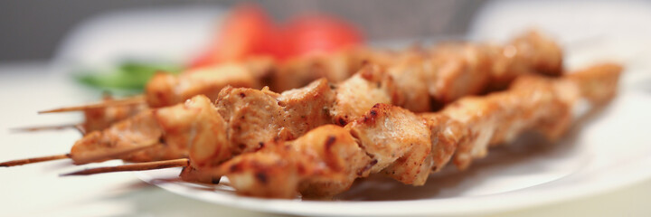 Close-up of delicious grilled chicken pieces on bamboo skewers on white plate. Aromatic meat for dinner. Home barbeque. Tasty meal and healthy food concept