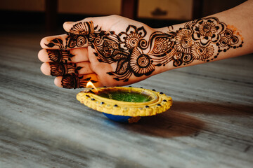 Close up shot of female hand with heena design and illuminating diya on diwali festival. Happy diwali