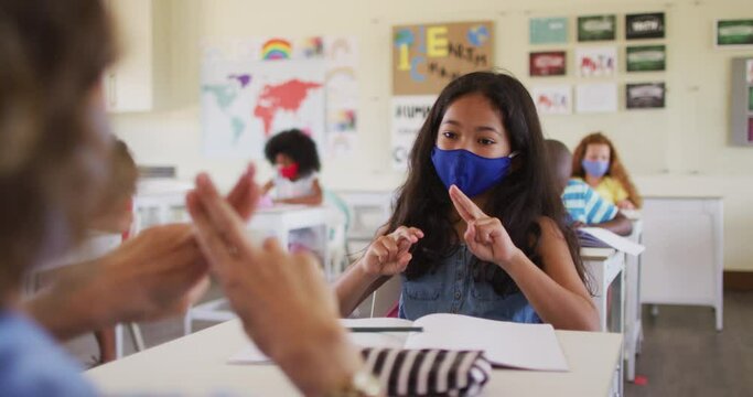 Female teacher and girl wearing face masks talking to each other through sign language in class