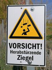 Schild mit der Aufschrift "Vorsicht herabst&uuml;rzende Dachziegel" an einer Ruine im Hafen von Magdeburg in Deutschland